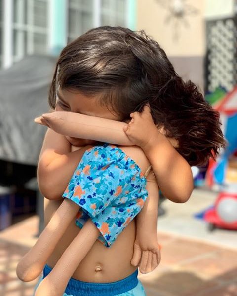 loving child with underdeveloped hand hugging their matching doll